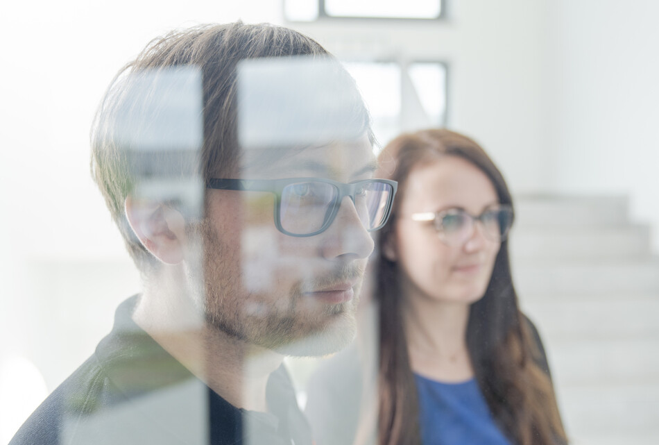 a men and a woman looking optimistic through a wall of glass.